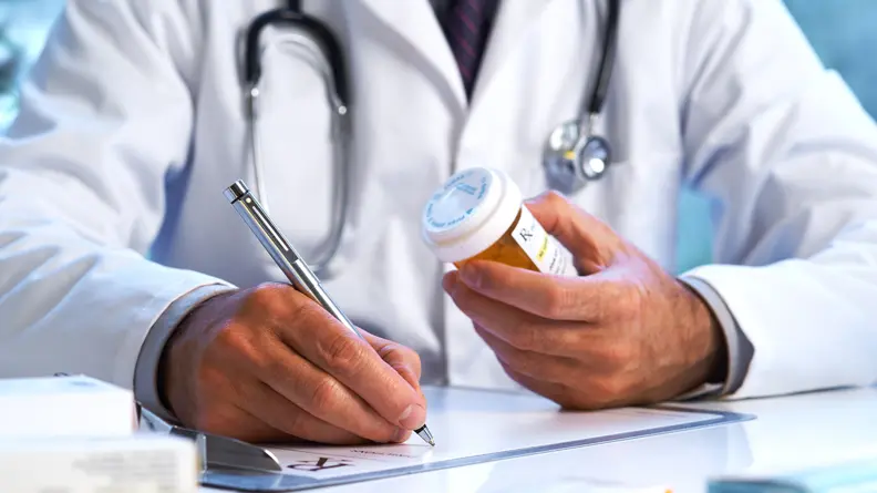 Image of a Doctor holding a medicine bottle and writing a prescription